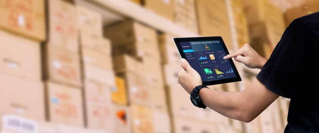 A warehouse worker reviewing inventory management software on a tablet.